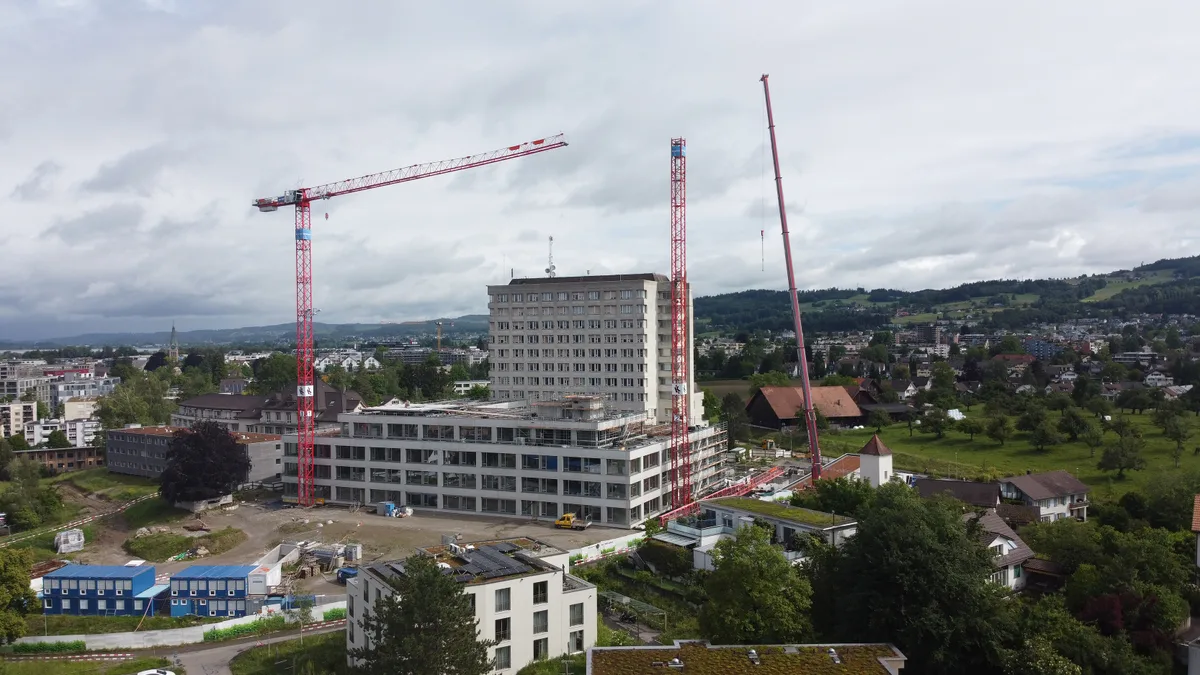 Zwei Krane stehen neben einem Betongebäude.